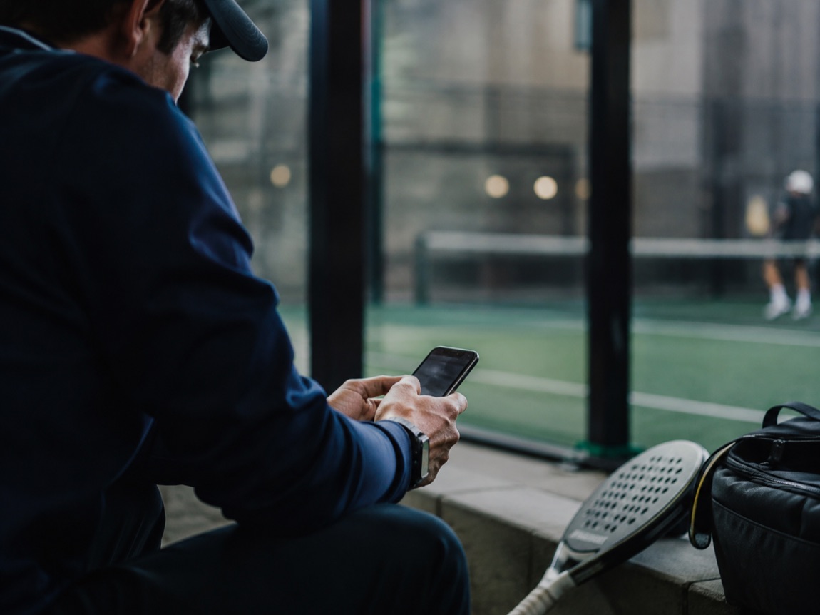 A player checking their phone courtside at a padel club